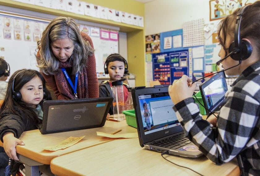Aula de primaria con estudiantes usando computadoras y tutoría digital