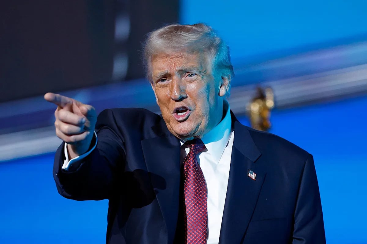 Hombre señalando con énfasis en evento político con fondo azul