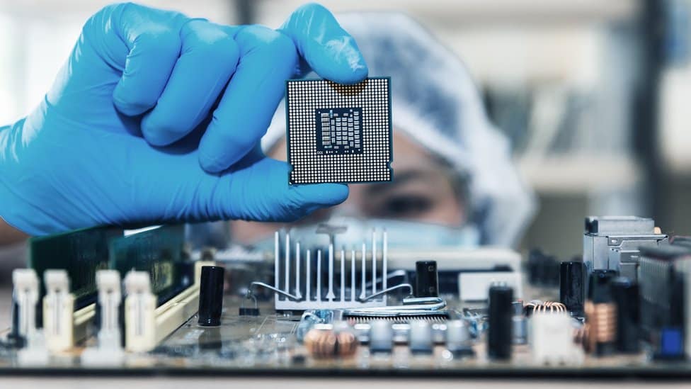 Microchip sostenido con guante azul en ambiente controlado de la industria de semiconductores