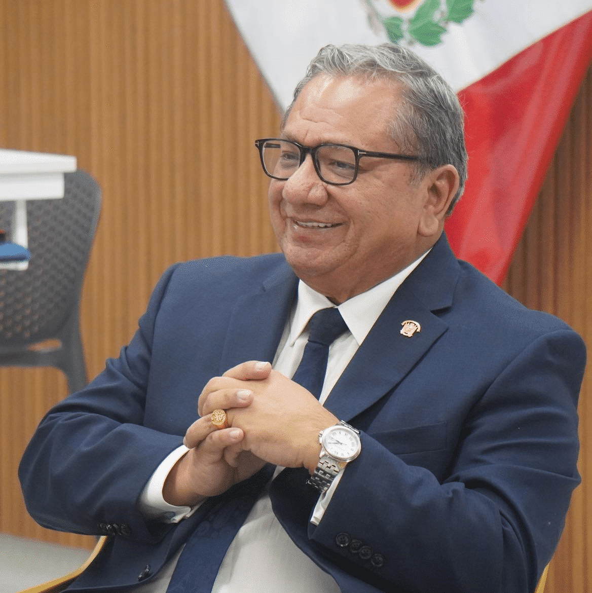 Carlos Anderson en traje oficial con bandera peruana de fondo
