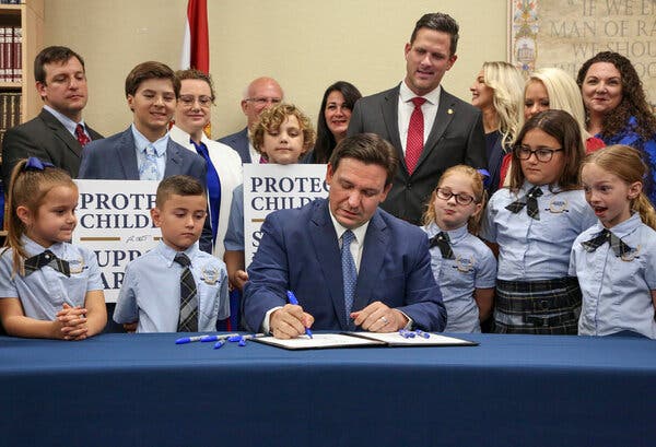 Evento formal de firma de legislaci&oacute;n educativa con ni&ntilde;os en uniformes y carteles de apoyo a padres e hijos
