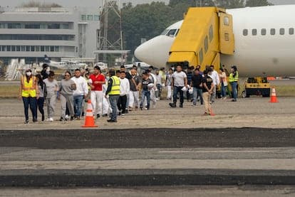 Personas caminando hacia un avi&oacute;n, aparentemente deportadas, en un aeropuerto