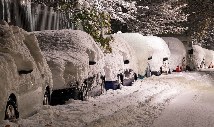 Veh&iacute;culos cubiertos de nieve en una calle urbana durante la noche