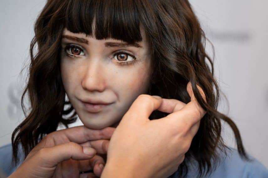 Primer plano de un robot humanoide realista con cabello oscuro, siendo ajustado por una persona