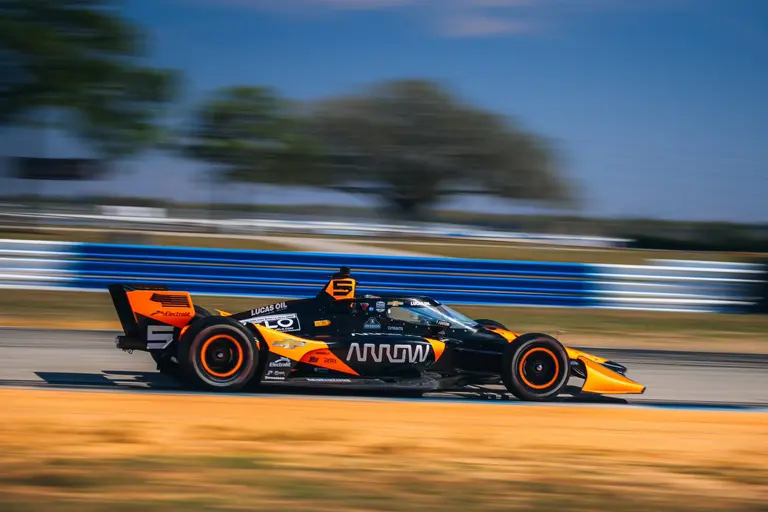 Coche de carreras IndyCar negro y naranja en pista