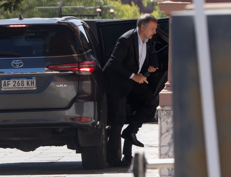 Hombre en traje negro saliendo de vehículo, en contexto político