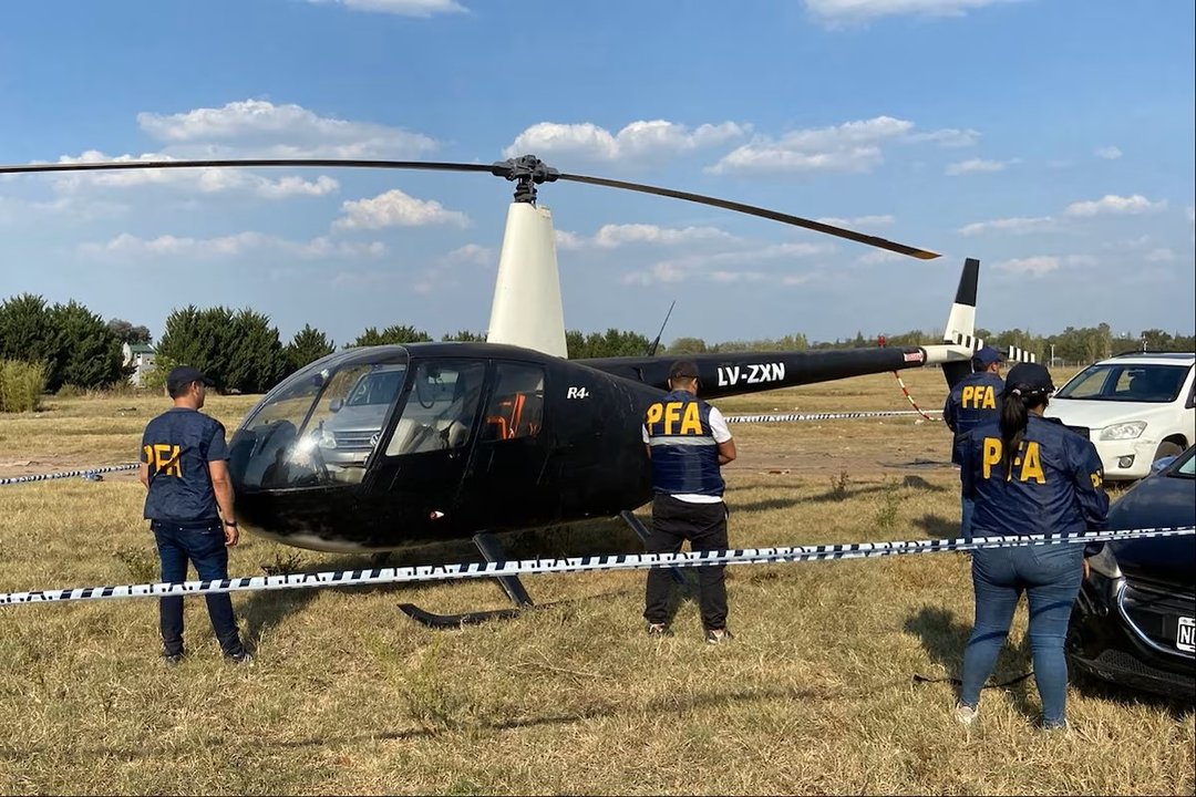 Helic&oacute;ptero de la Polic&iacute;a Federal Argentina en un campo, con personal de la PFA observando
