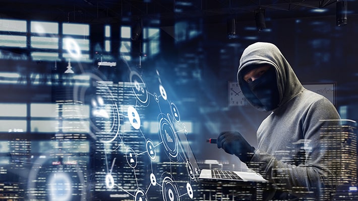 Persona con pasamontañas trabajando en laptop, representando ciberdelincuencia y malware ATM