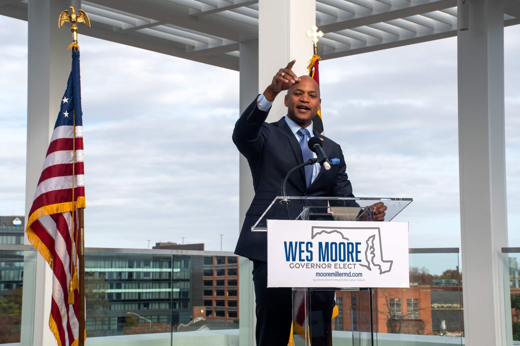 Wes Moore hablando en un podio con cartel de Gobernador Electo, con banderas de EE.UU. y Maryland al fondo