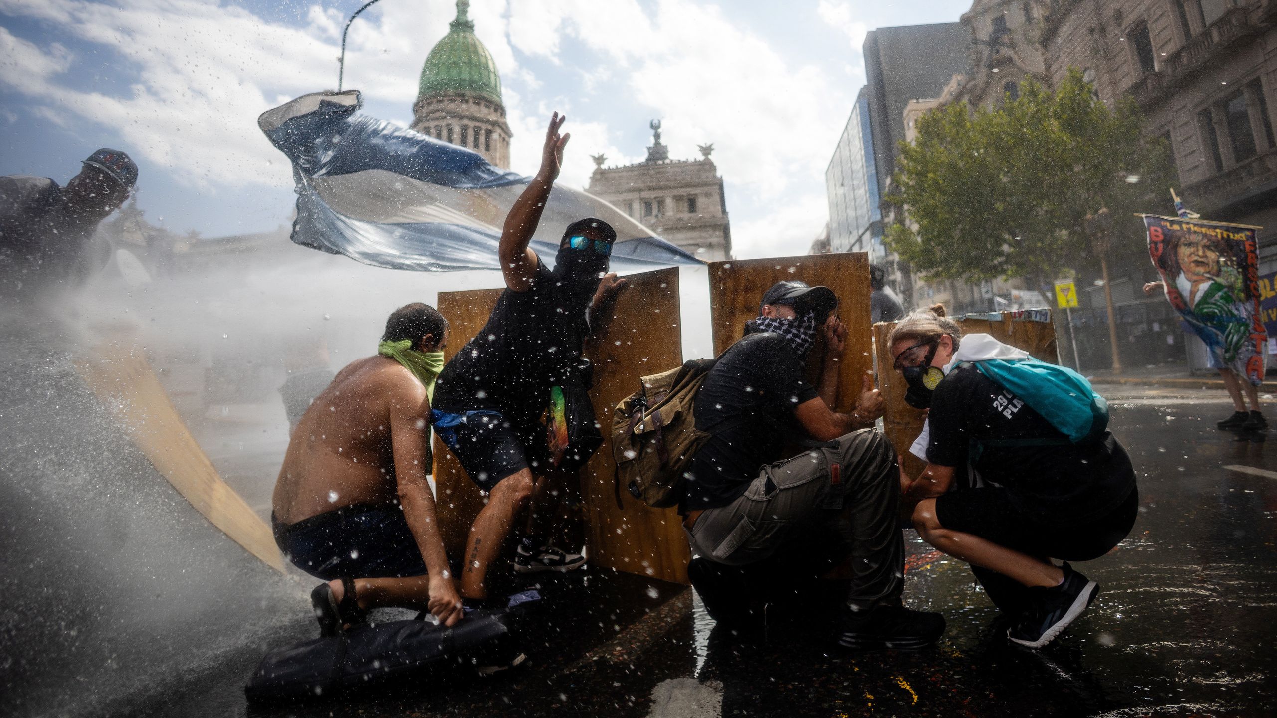 Manifestantes en una marcha en Argentina usando barricadas de madera mientras son rociados con agua