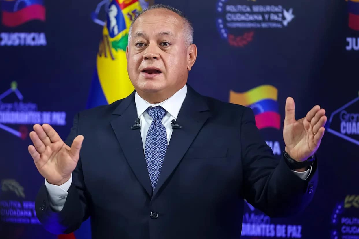 Contexto político oficial en Venezuela, hombre con traje oscuro gesticula frente a símbolos nacionales