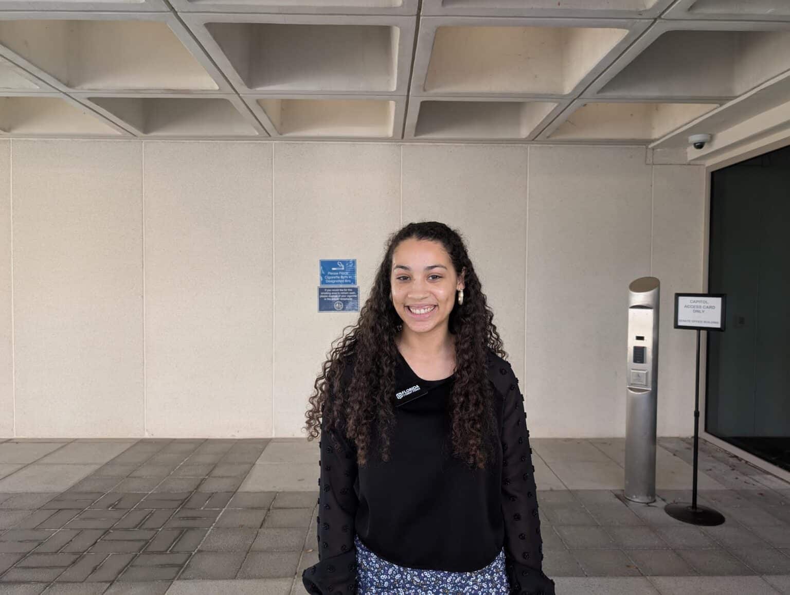 Mujer frente a edificio gubernamental con letrero 'CAPITOL ACCESS CARD DESK'