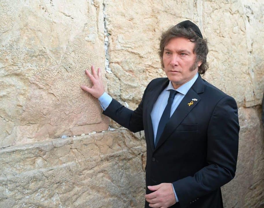 Javier Milei en un momento solemne en Israel, tocando un muro de piedra y vestido con traje oscuro y kip&aacute;.