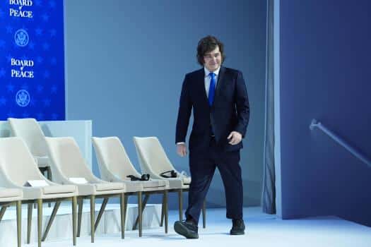 Javier Milei en un evento formal, con traje oscuro y corbata azul, acerc&aacute;ndose a un podio