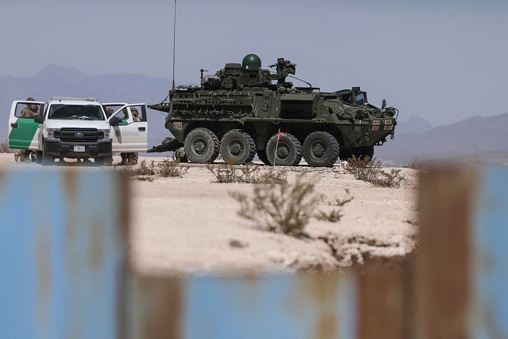 Veh&iacute;culo militar estacionado en zona des&eacute;rtica con personal de seguridad en fondo monta&ntilde;oso