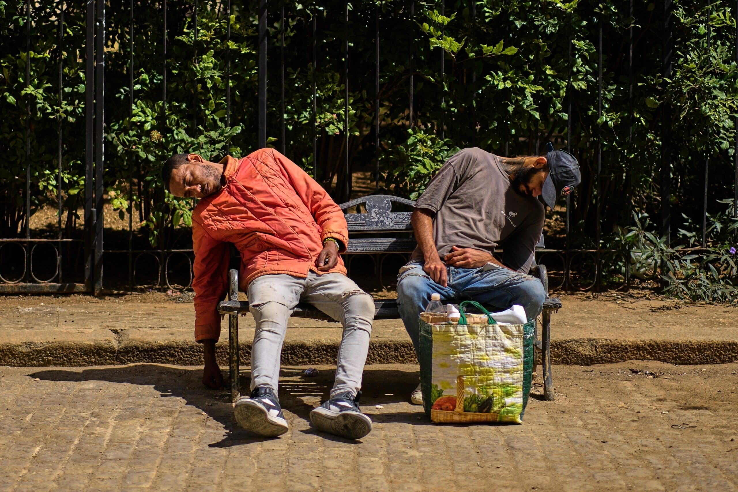 Dos hombres descansando en un banco urbano, ilustrando desaf&iacute;os socioecon&oacute;micos