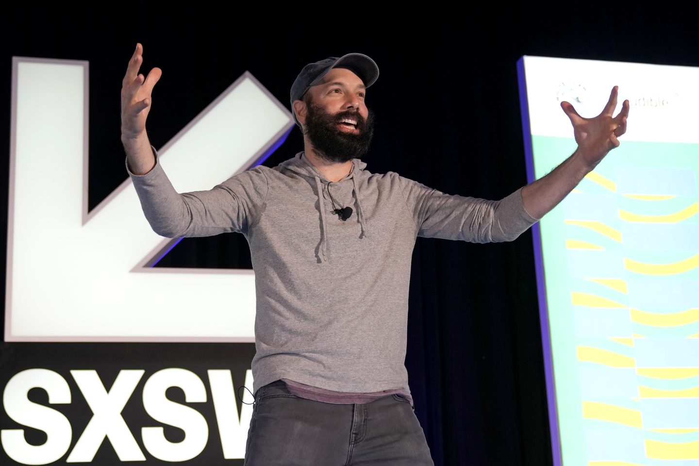 Jack Conte hablando con entusiasmo en el escenario de SXSW, vistiendo una sudadera gris y gorra