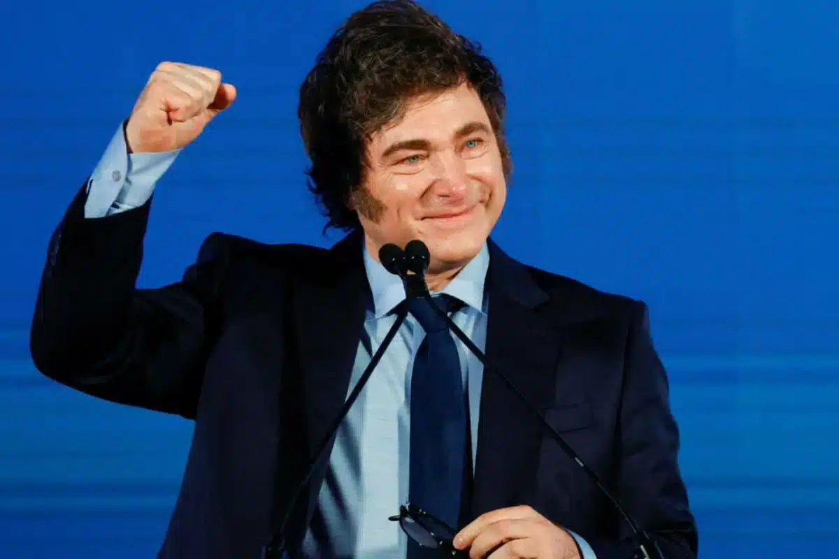 El presidente Javier Milei en un gesto de celebraci&oacute;n, con traje oscuro y fondo azul