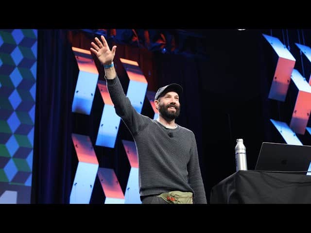Jack Conte interact&uacute;a con la audiencia en una charla, sonriendo y con una botella de agua en la mesa