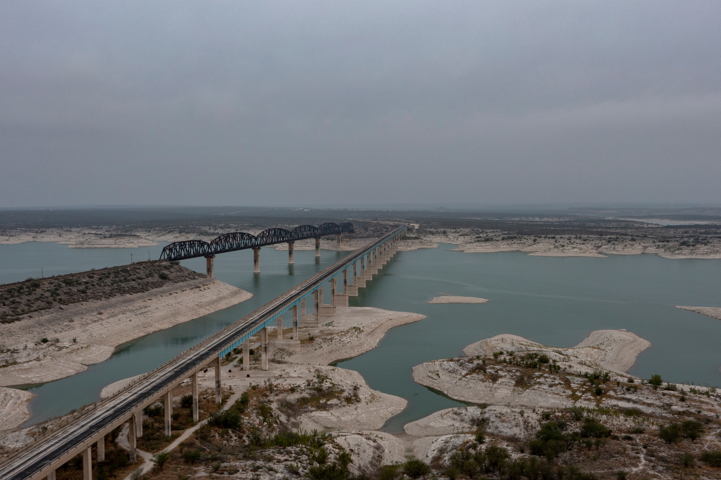 Puente ferroviario oscuro sobre un cuerpo de agua en un paisaje des&eacute;rtico