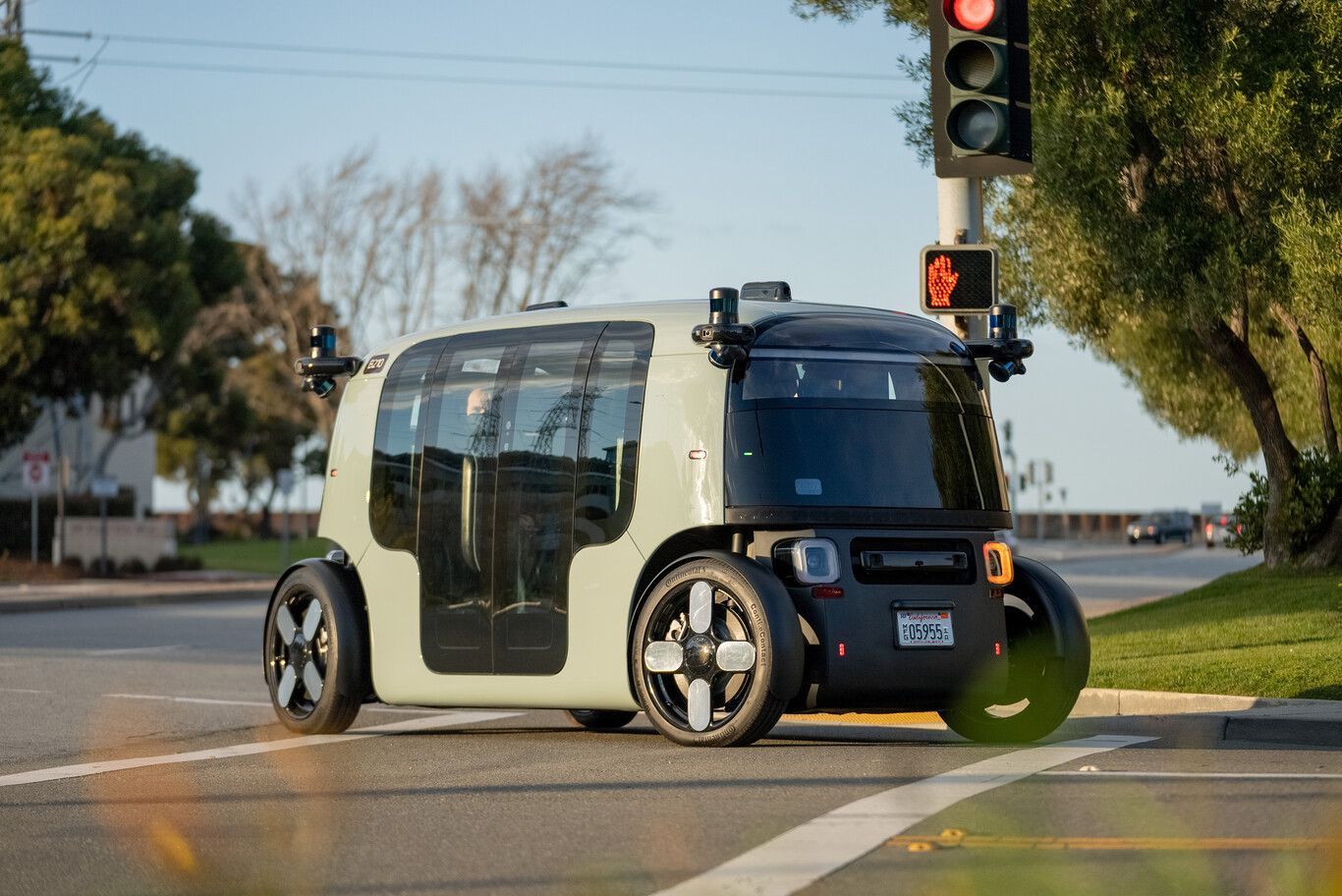 Vehículo autónomo futurista circular con grandes ventanales, circulando en una calle con semáforo en rojo