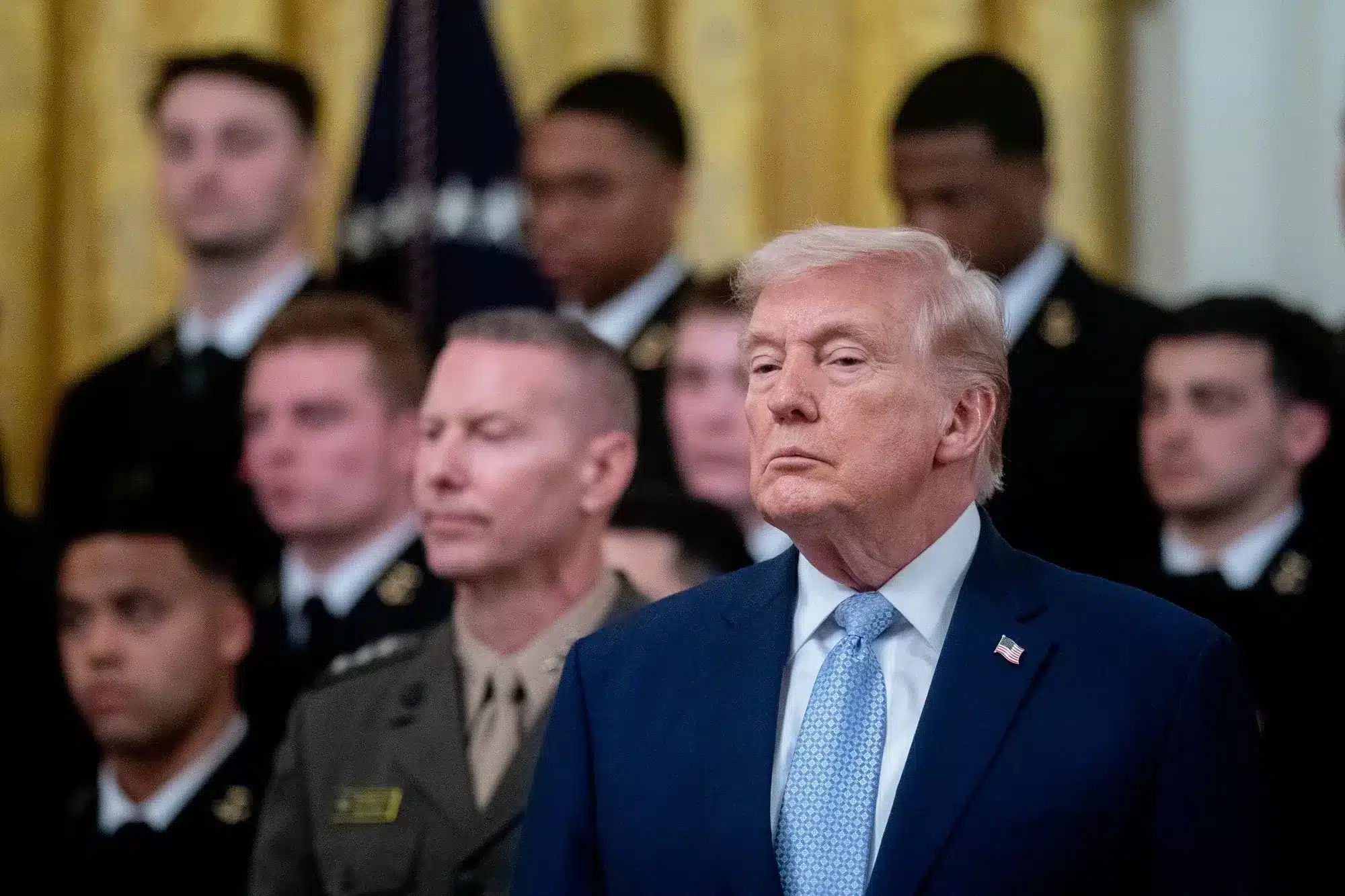 Grupo de hombres en un entorno ceremonial, posiblemente en la Casa Blanca, con un hombre de cabello claro y uniformados militares
