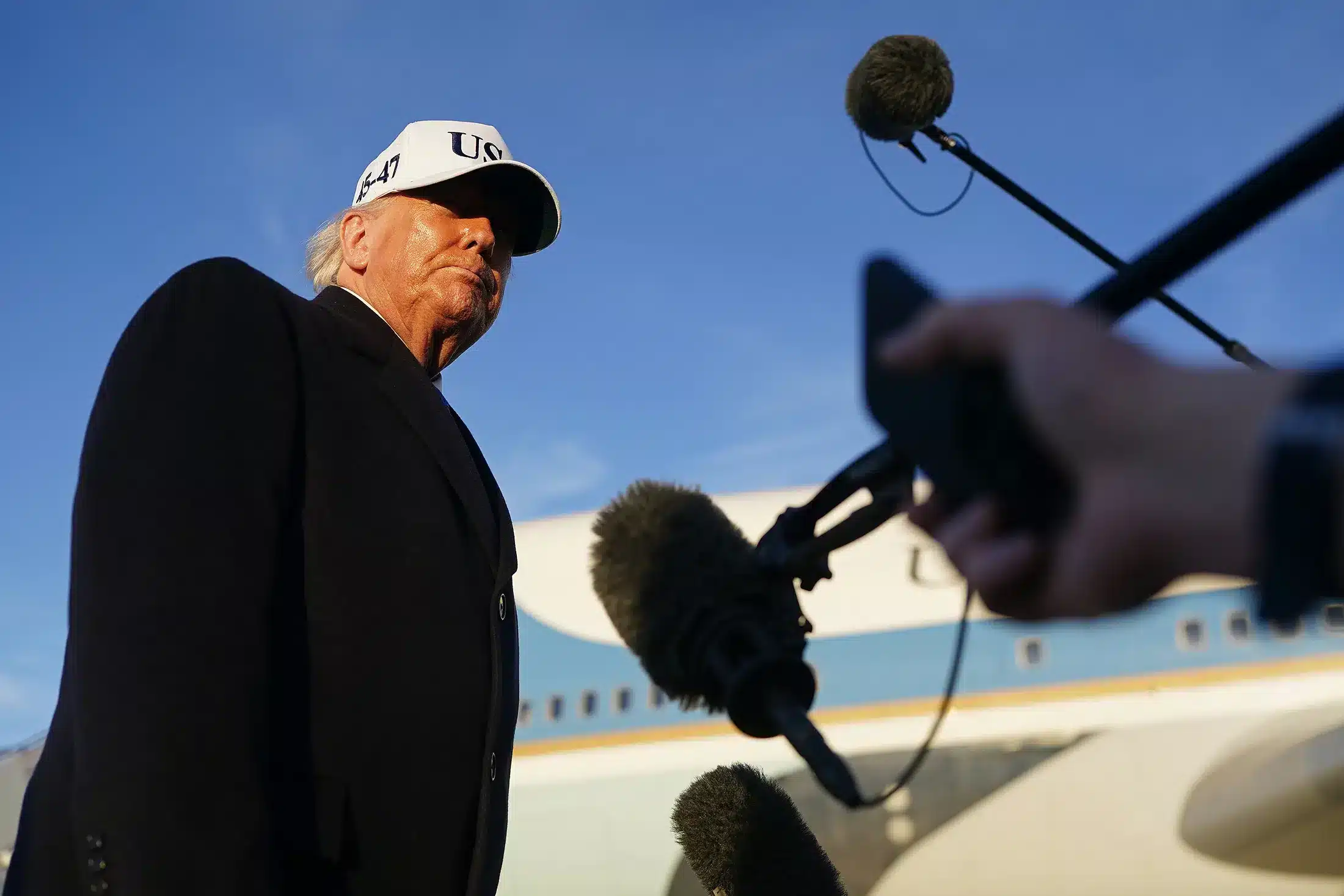 Funcionario estadounidense con gorra U.S. frente a un avión y periodistas