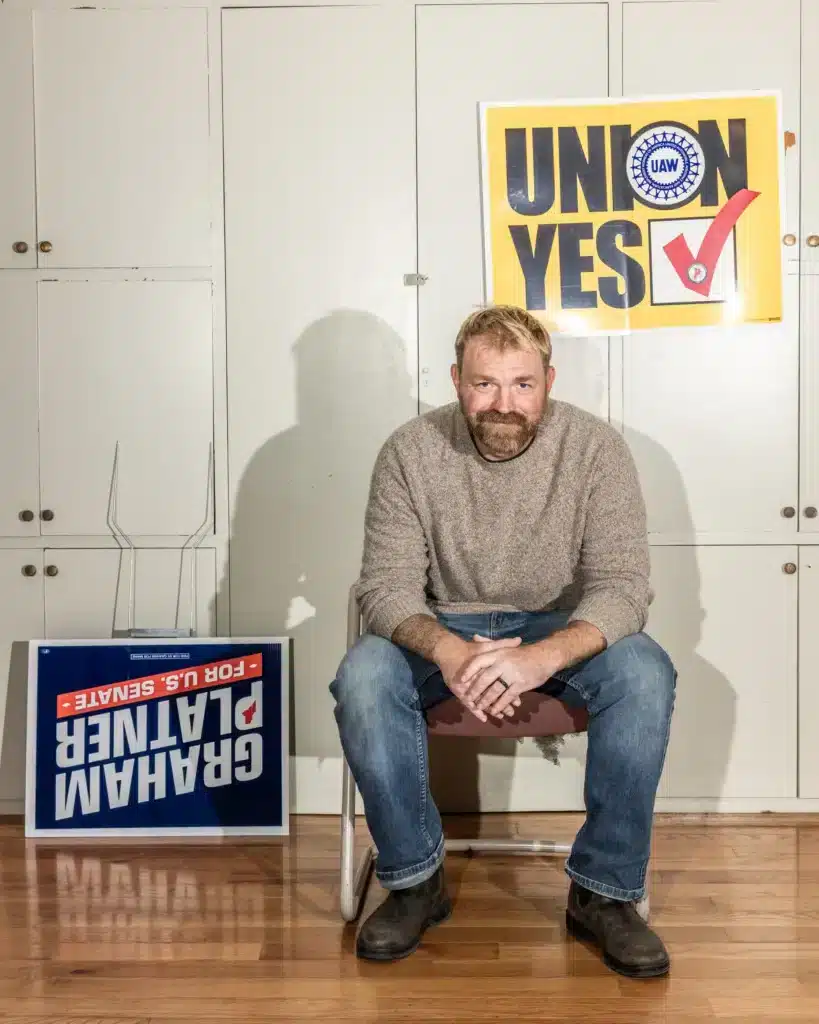 Graham Platner sentado junto a un cartel de unión sindical y su nombre de campaña