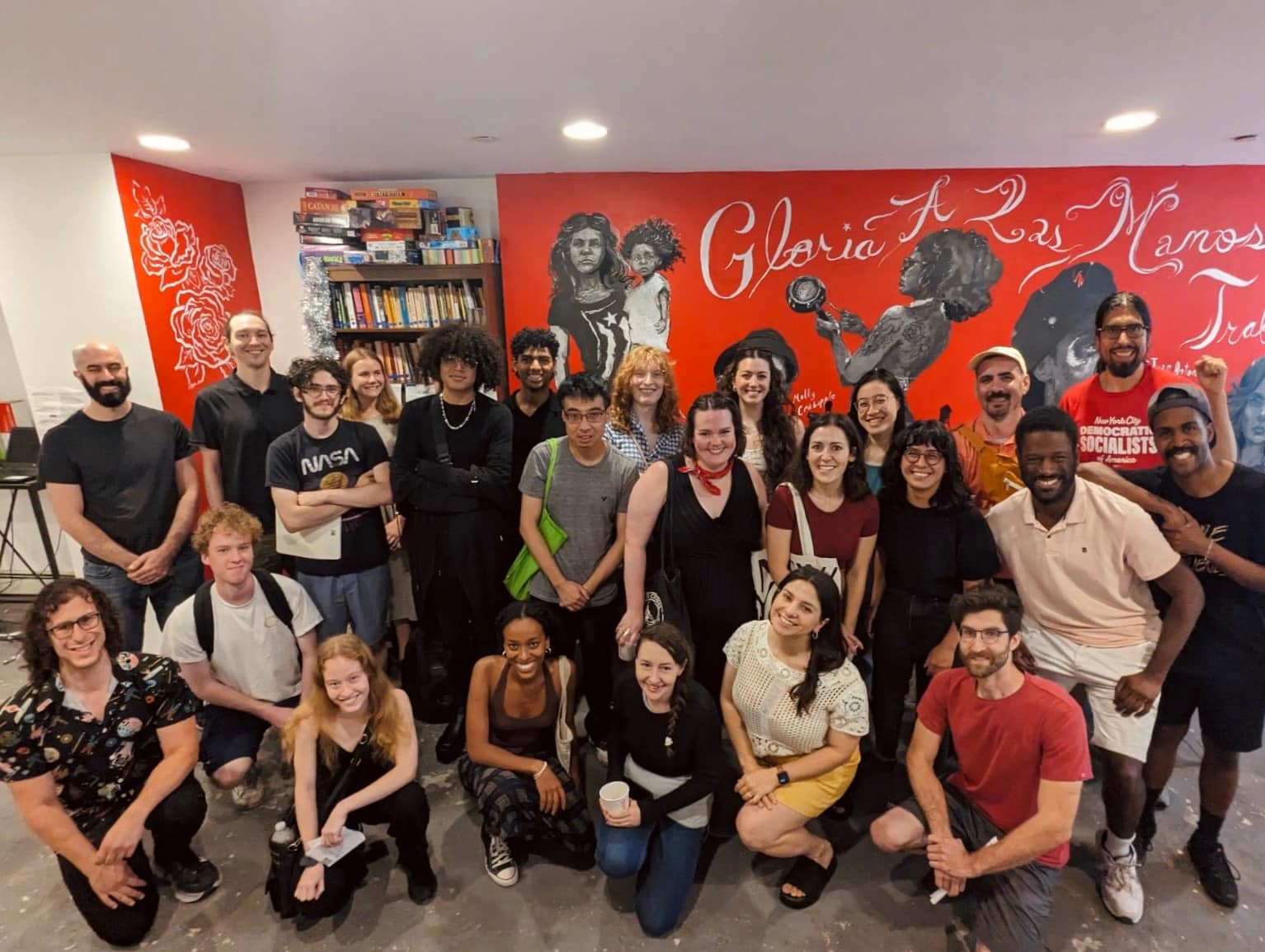 Grupo diverso en reunión comunitaria de DSA en Nueva York, con mural rojo y pancartas