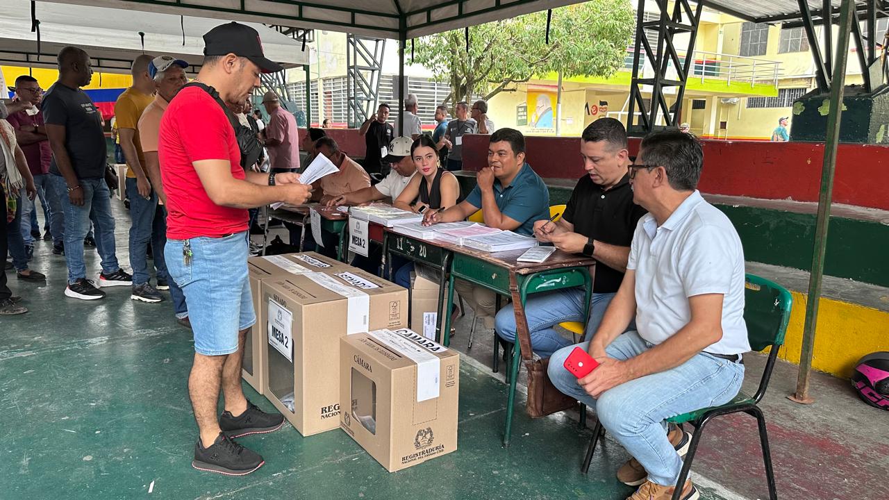 Sitio de votación con personas en fila y funcionarios electorales