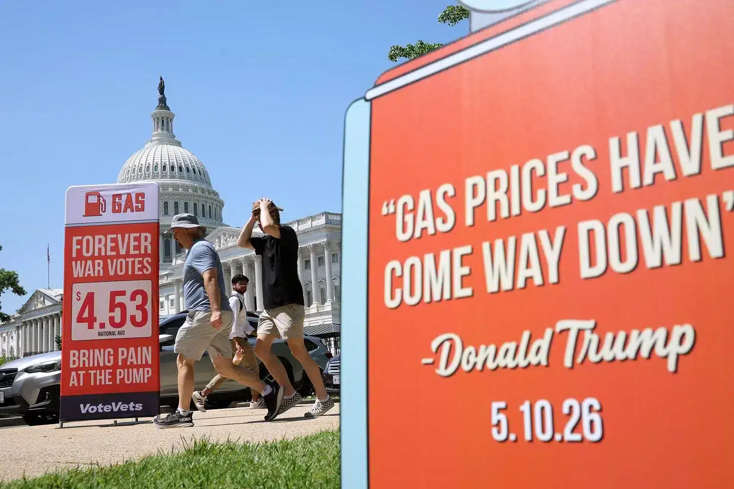 Personas caminando frente al Capitolio de Estados Unidos con carteles sobre precios de gasolina y críticas a políticos