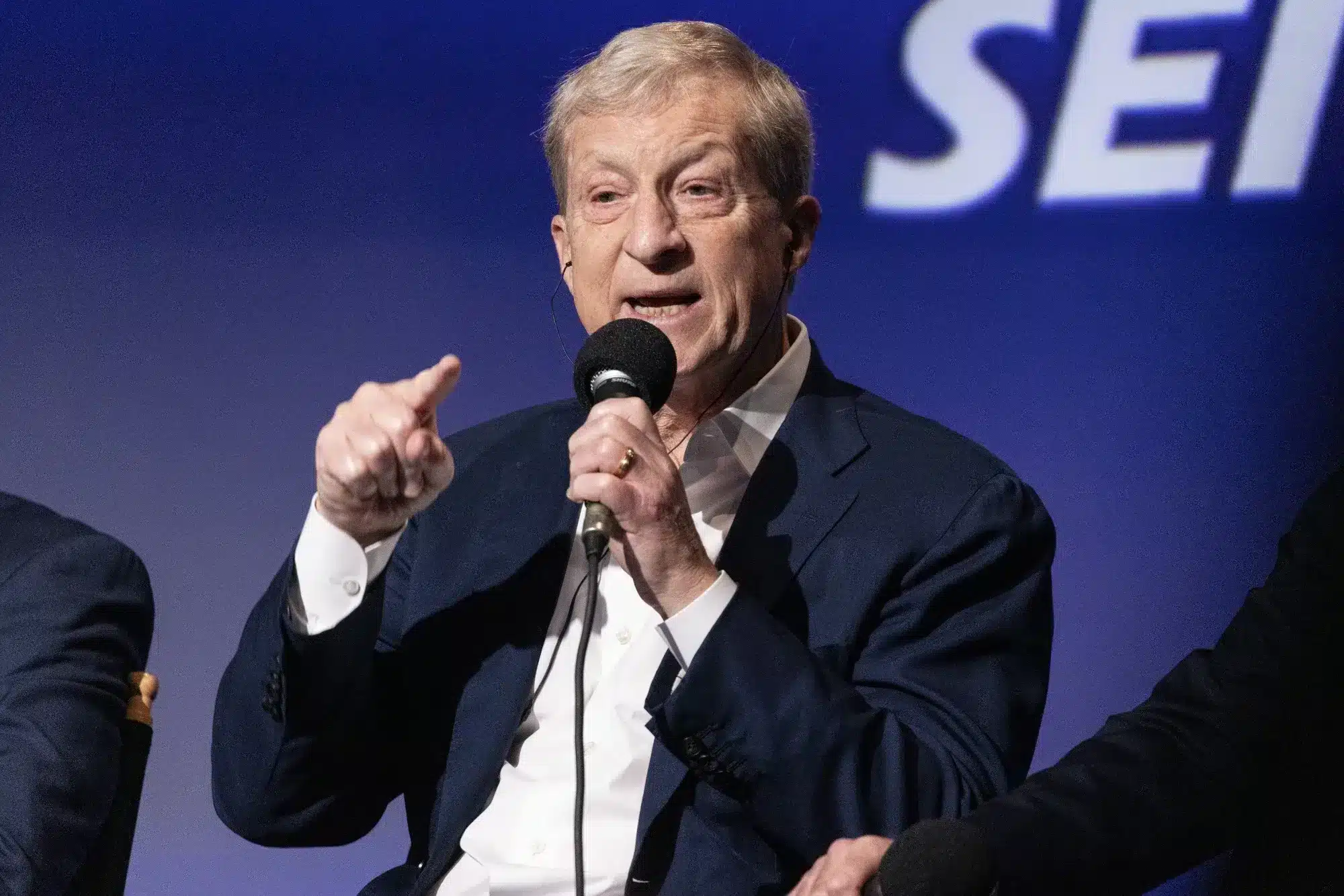 Tom Steyer hablando apasionadamente en un evento político, señalando con el micrófono