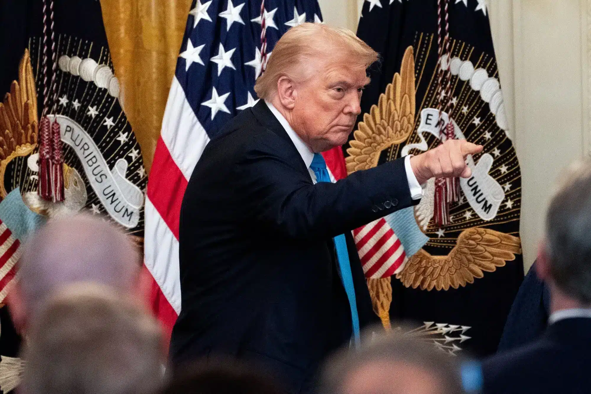 Trump señalando enérgicamente durante un discurso oficial con banderas estadounidenses de fondo