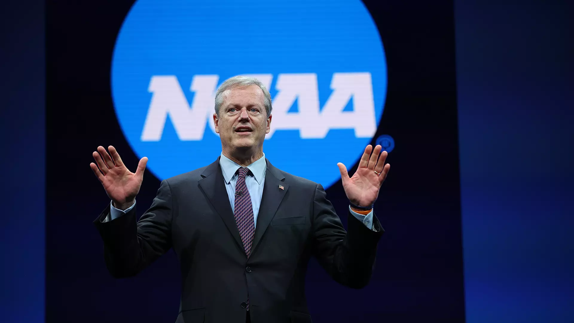 Charlie Baker en un escenario con el logo de la NCAA de fondo