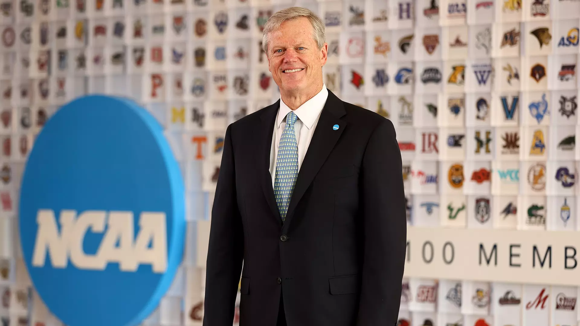 Charlie Baker de pie frente a una pared con logotipos de la NCAA