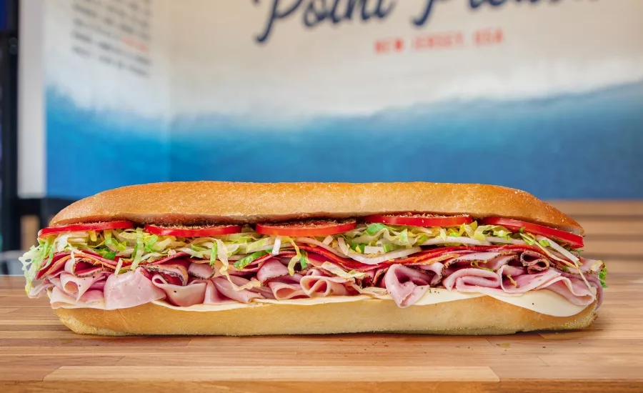 Sándwich submarino de Jersey Mike's servido sobre una tabla de madera, con un cartel de Point Pleasant, New Jersey