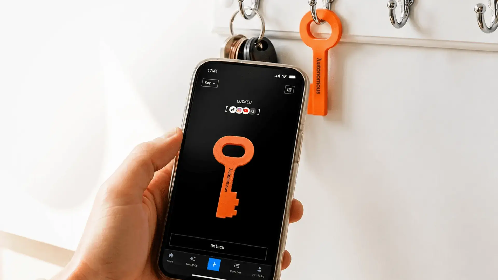 Mano sosteniendo un teléfono con aplicaciones bloqueadas y una llave naranja en un llavero