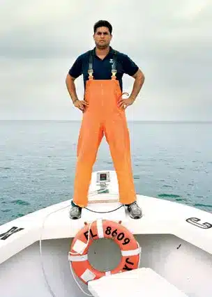 Roger Duarte, el Rey del Cangrejo de Miami, de pie en la proa de un bote con overol naranja