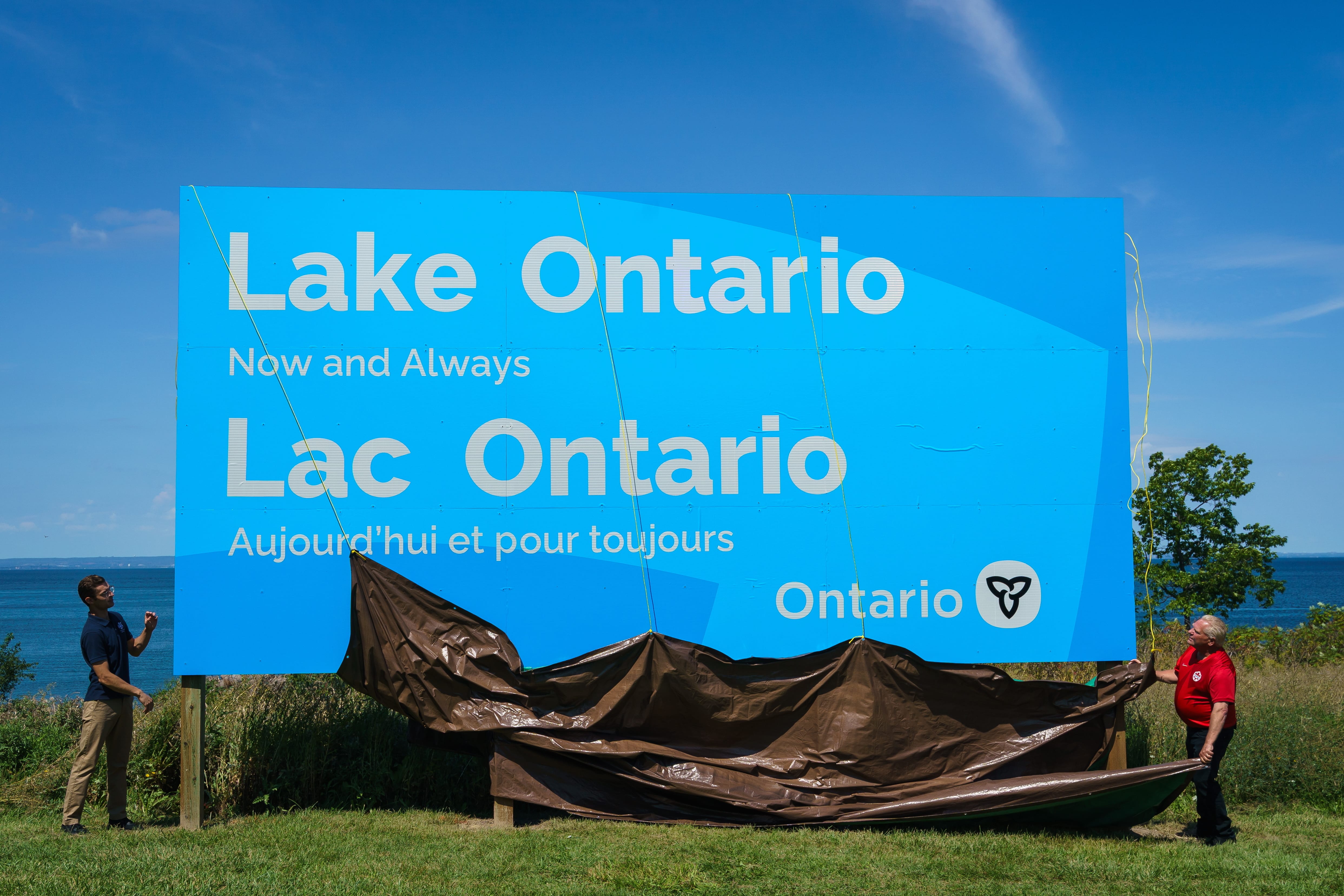 Personas junto al cartel bilingüe del Lago Ontario