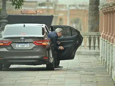 Hombre con traje bajando de un automóvil gris frente a un edificio gubernamental