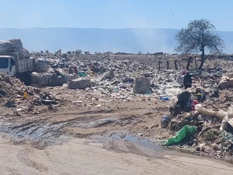 Terreno de la planta de residuos de El Pantanillo con montículos de basura, un camión y montañas al fondo