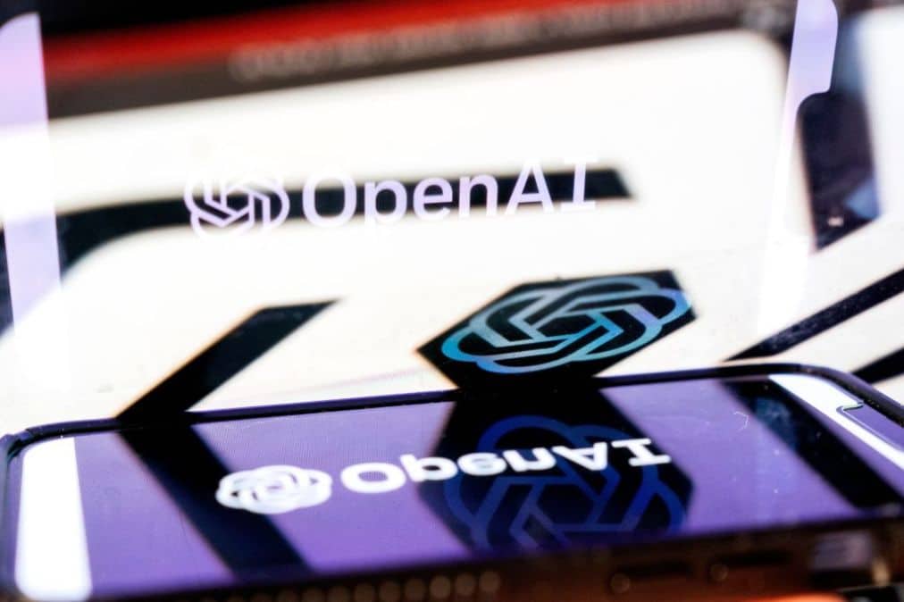 Logotipo de OpenAI reflejado en una superficie junto a un teléfono móvil
