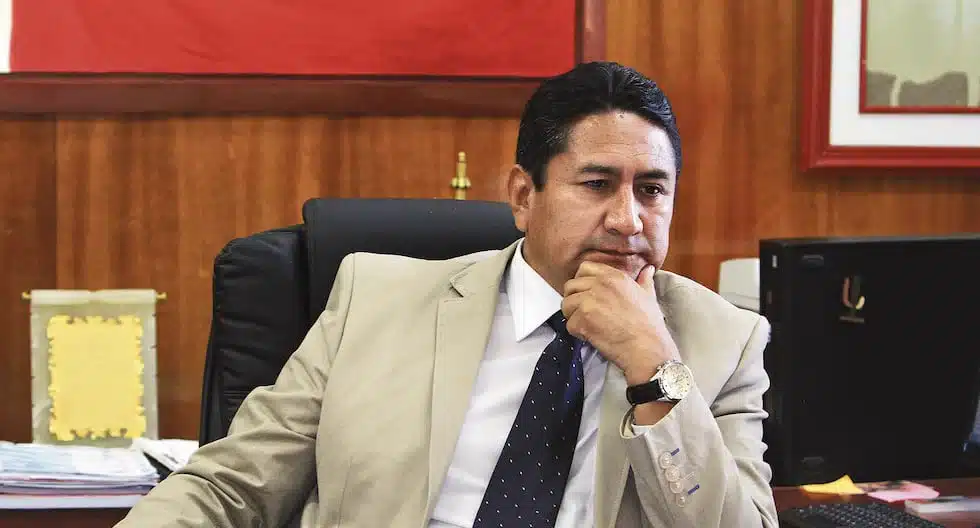 Hombre sentado en una oficina con traje claro y fondo con bandera, en contexto del Poder Judicial