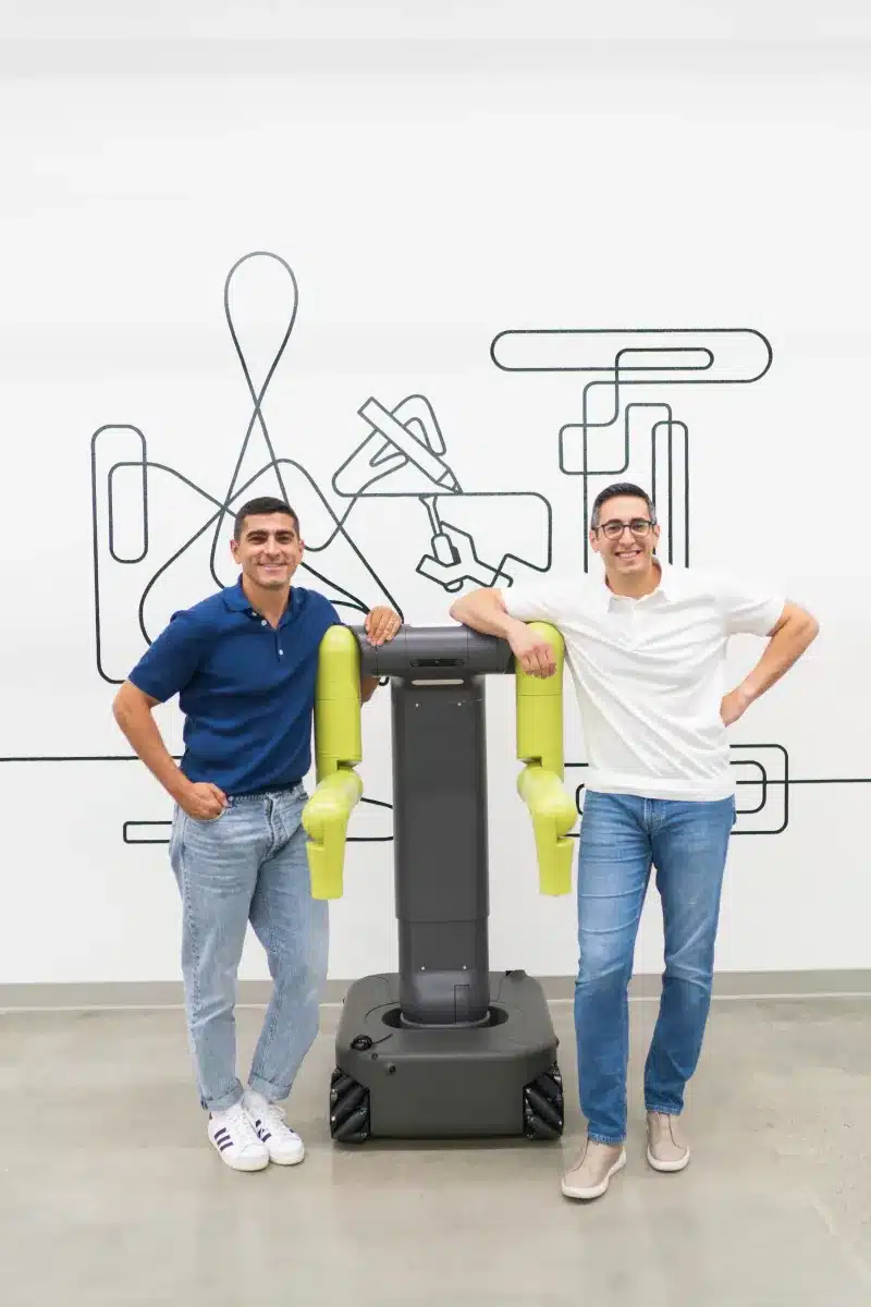 Equipo de Maven Robotics junto a un robot de brazos verdes en sus instalaciones