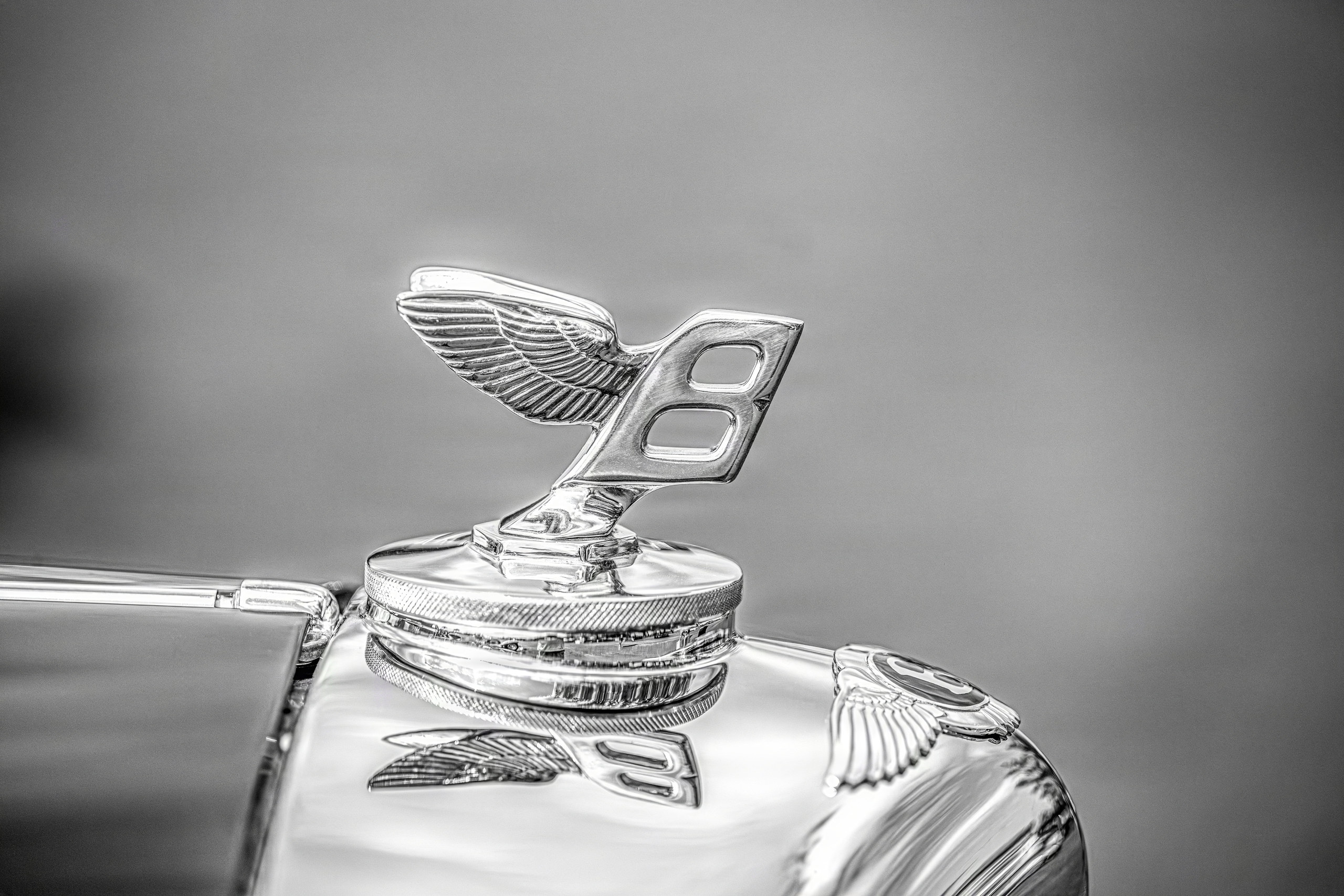 Winged chrome hood ornament mirrored in polished coachwork, monochrome — fine art photography on aluminum