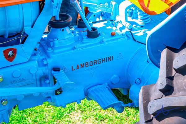 Close-up of a blue-painted tractor gearbox with raised LAMBORGHINI lettering in rust red, a bull shield badge at left and a lugged rear tyre at right.