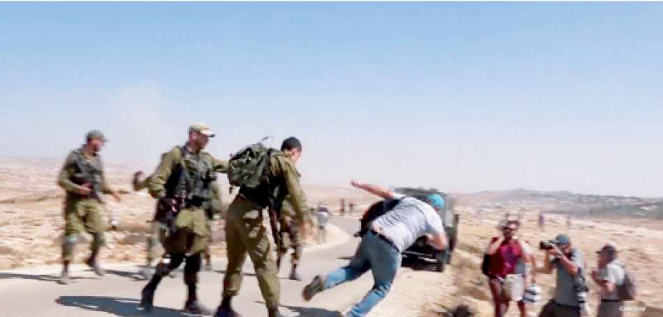 ناشط يساري لحظة قبل سقوطه بعدما دفعه ضابط من الاحتلال خلال إحدى المسيرات المنددة بالاستيلاء على أراضي الفلسطينيين بالضفة المحتلة-(أرشيفية)