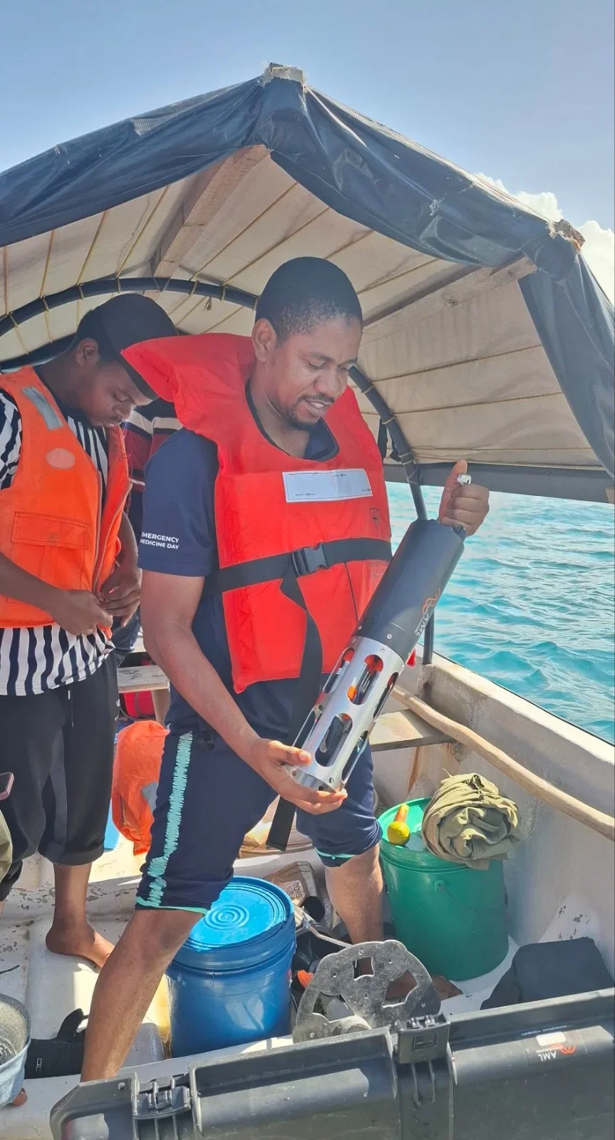A researcher in a life jacket holds an AML CTD aboard a small boat under a canopy.