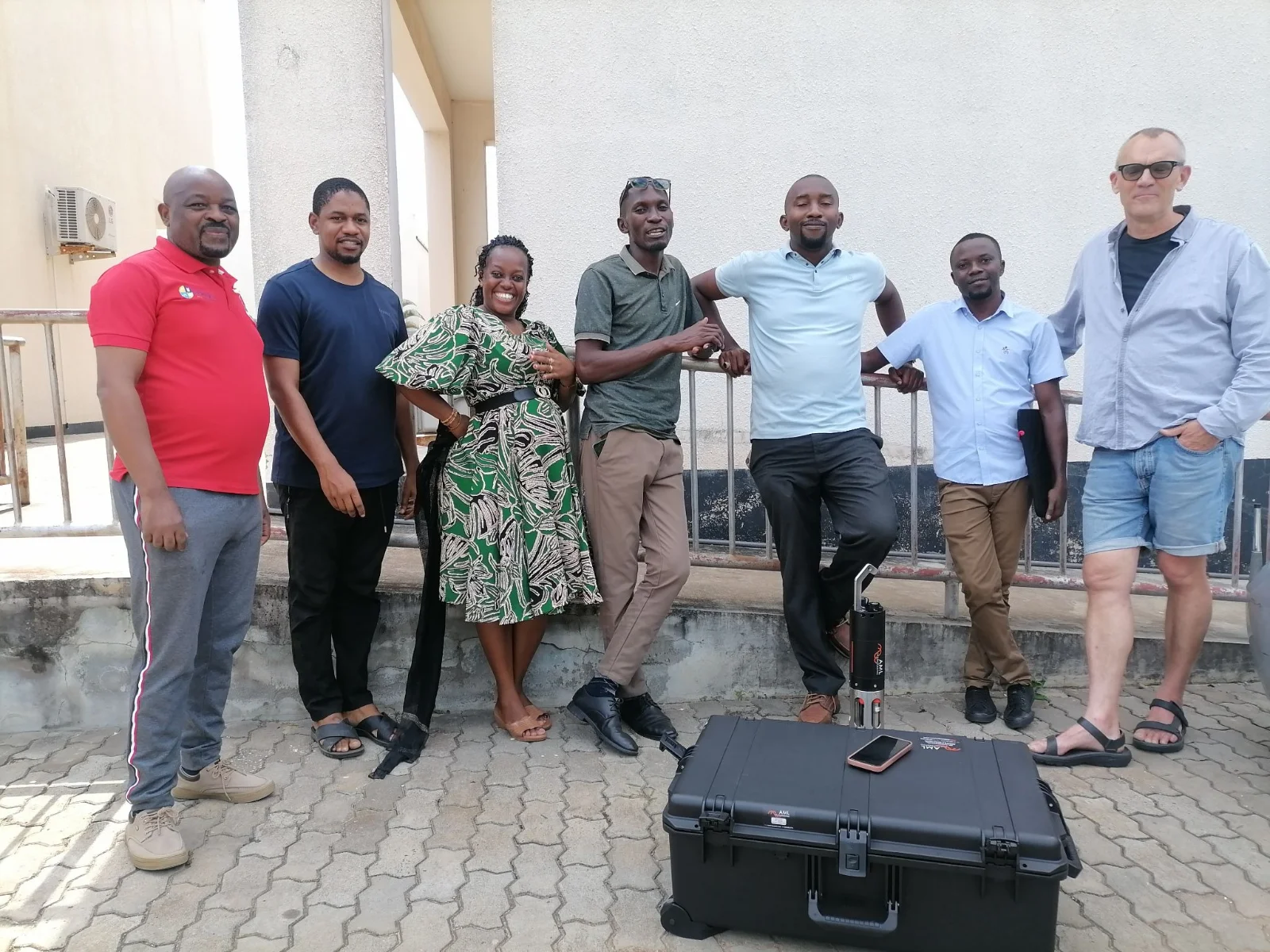 Members of the research team standing outdoors beside an AML instrument and its transit case.