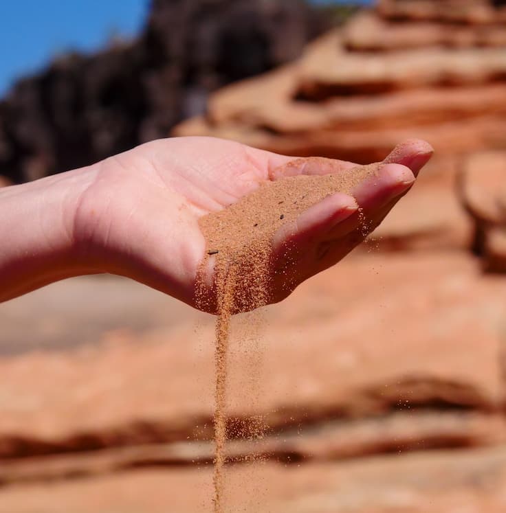 Handful of sand slips through a person hand